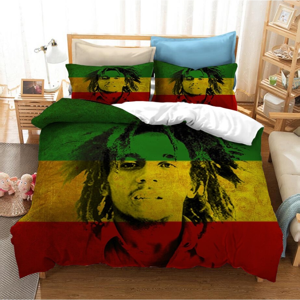 Dans une chambre le lit est décoré d'une parure à l'effigie de Bob Marley jeune avec les dreadlocks court, l'ensemble est de couleur rouge, jaune et vert, avec le visage de bob marley en noir, les coussins sont assortis, à droite du lit il y a un banquette en bois avec les coussins blanc, et un meuble étagère en bois, à gauche du lit il y a une table de chevet en bois et des jouets