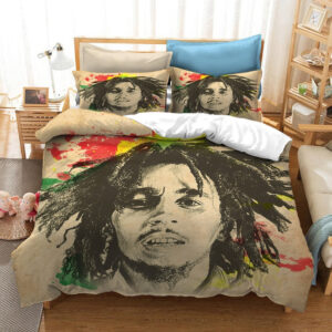 Dans une chambre le lit est décoré d'une parure à l'effigie de Bob Marley dessiné comme au fusin, de couleur beige avec des touches de couleurs, avec le visage du chanteur bob marley dessiné au fusin, les coussins sont assortis, à droite du lit il y a un banquette en bois avec les coussins blanc, et un meuble étagère en bois, à gauche du lit il y a une table de chevet en bois et des jouets