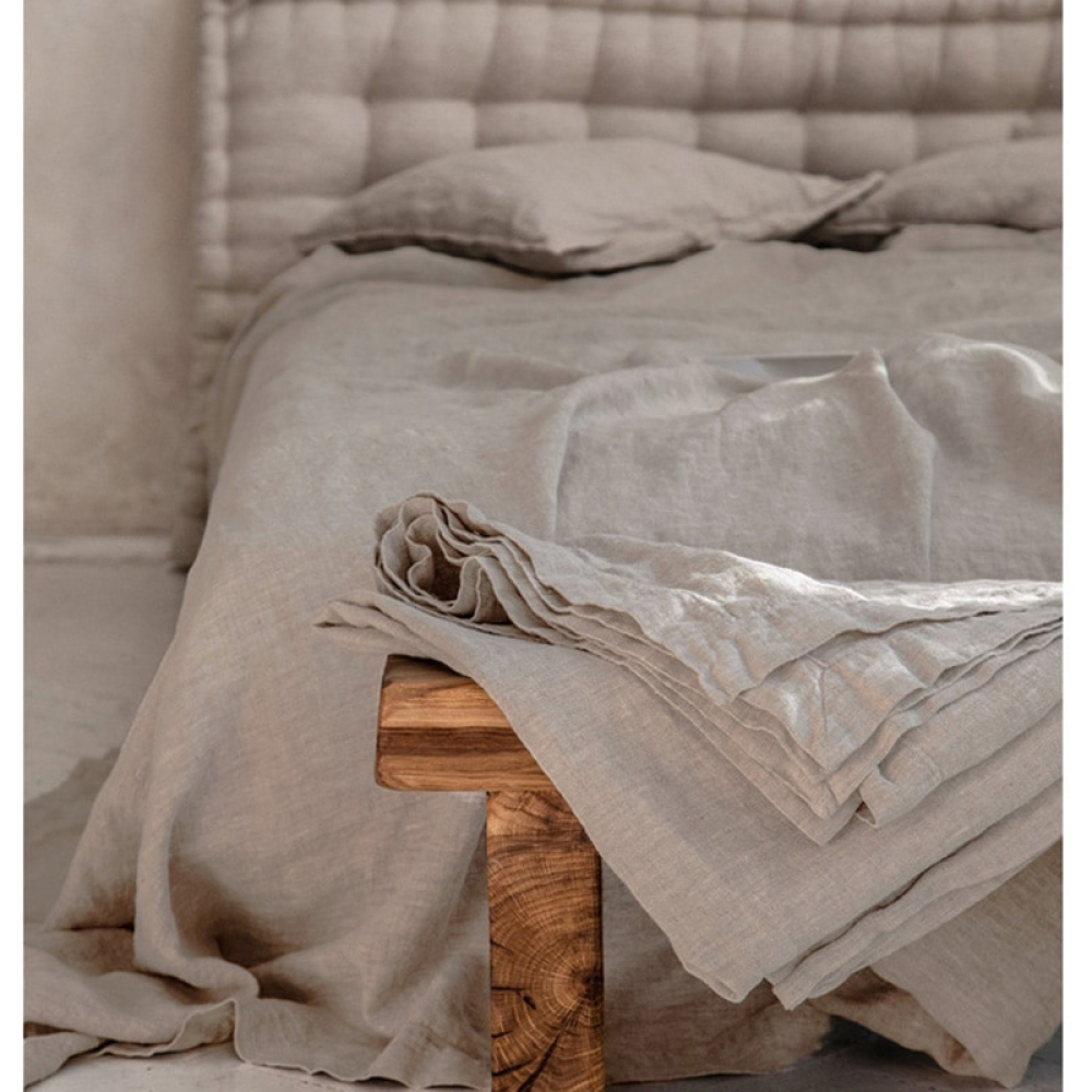Dans une chambre, couverte d'une parure de lit drapée, devant le lit se trouve un banc en bois sur lequel est posé des draps pliée de la même couleur; et une tête de lit moltonnée complète la chambre