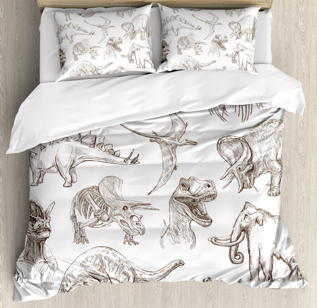 Dans une chambre le lit est décoré d'une parure avec plusieurs de dinosaures dessinés finement, le reste de la couverture est blanche, les coussins sont assortis, à droite du lit il y a un banquette en bois avec les coussins blanc, et un meuble étagère en bois, à gauche du lit il y a une table de chevet en bois et des jouets