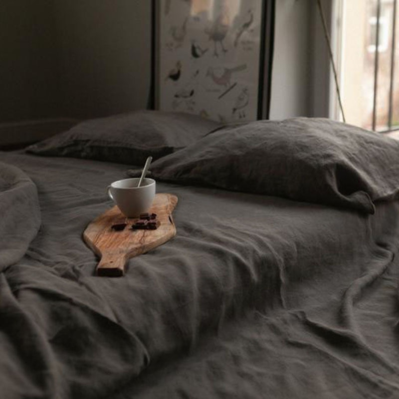Dans une chambre le lit est recouvert d'une belle parure de lit en lit gris, avec les oreillers assorties , sur le lit est posée une petite planche de bois sur laquelle il y a une taille de boisson chaude