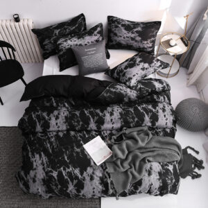 Parure de lit scandinave de type marbre de couleur noire et grise avec un livre ouvert dessus avec un coussin gris et une chaise noire à côté