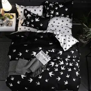Parure de lit scandinave au motif d'hirondelle noire et blanche avec un drap gris et un livre ouvert posés dessus