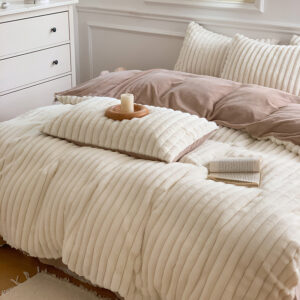 Parure de lit de couleur beige polaire avec livre ouvert dessus et un coussin avec un bougie sur un socle en bois
