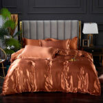Parure de lit en satin de couleur orange unie avec une tasse de café posée dessus devant un mur noir et un sol noir