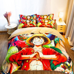 Parure de lit One piece multicolore où l'on voit le personnage Monkey D. Luffy les mains jointes, cette parure est installée sur un lit dans une chambre avec une table de chevet ronde à gauche et une table de chevet carrée avec une lampe dessus à droite