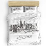 Parure de lit New York noire et blanche effet dessin avec "New York" écrit en dessous. Sur un lit double avec deux coussins assortis. La tête de lit est en bois beige. Sur fond blanc.