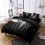 Parure de lit avec araignée de Spiderman blanche et grise sur fond noir. L'ensemble est sur un lit double avec des coussins assortis à la housse de couette.La décoration de la chambre est épurée dans les tons beige et blanc. Un tapis gris anthracite sur le coin droit de la photo.