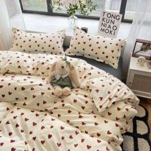 Parure de lit beige imprimés coeurs rouges sur un lit deux personnes. Une fenêtre en tête de lit et une table de chevet à droite.