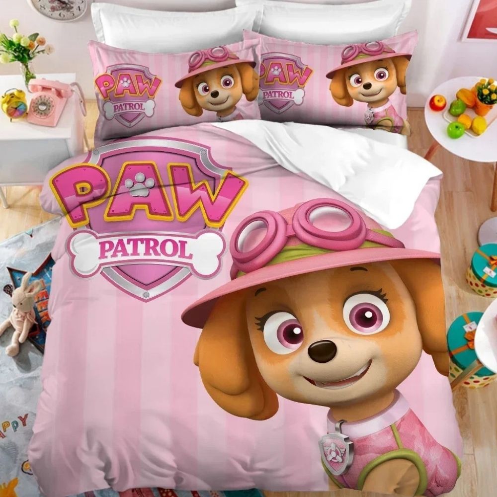 Parure de lit Pat'Patrouille rose avec Stella sur le coin droit et le logo de la Pat'Patrouille en haut à gauche. Les deux coussins sont assortis à la housse de couette. Sur un lit double dans une chambre avec une table de chevet à gauche et une petite table ronde blanche à droite.