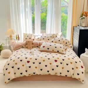 Parure de lit romantique beige avec des petits coeurs bleus et marrons et des petits chiens blancs. La parure est sur un lit deux places avec les taies d'oreillers assorties. Le lit se trouve devant une grande fenêtre avec des voilages blancs. A droite, un meuble noir, à gauche, une table de chevet en métal avec une lampe de chevet allumée.