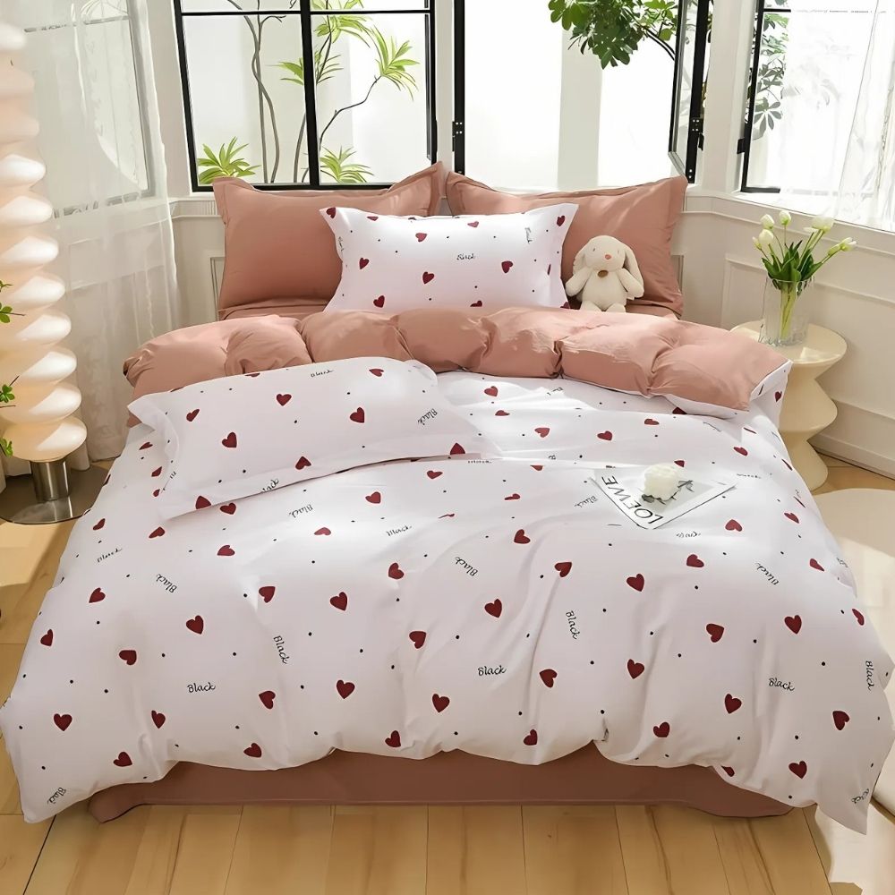 Parure de lit romantique beige et blanche à coeurs sur un lit double avec des cœurs rouges et des écritures noires sur fond blanc. Les coussins sont assortis. Des fenêtres se trouvent au-dessus du lit.
