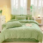 Parure de lit unie en polaire verte aux motifs effet tricotés composée d'une housse de couette et de coussins assortis posés sur un lit double. La tête de lit est contre une fenêtre, un petit meuble blanc à gauche.