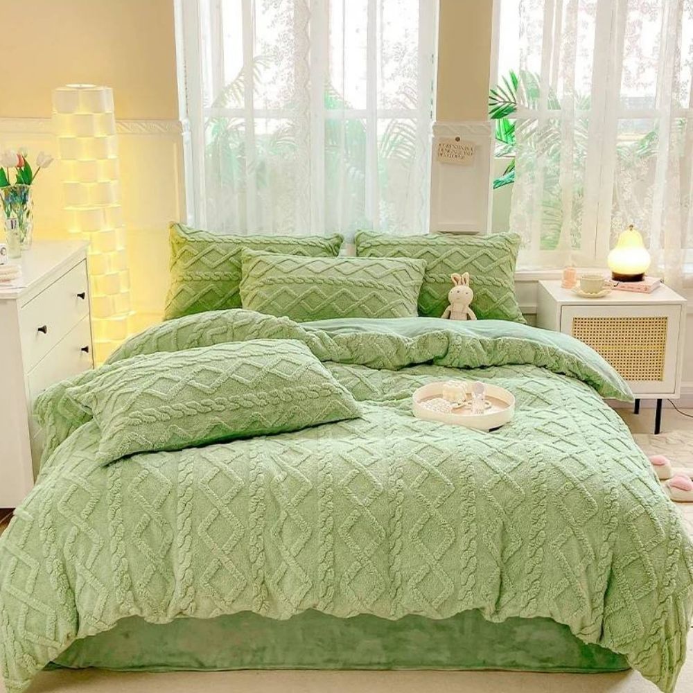 Parure de lit unie en polaire verte aux motifs effet tricotés composée d'une housse de couette et de coussins assortis posés sur un lit double. La tête de lit est contre une fenêtre, un petit meuble blanc à gauche.