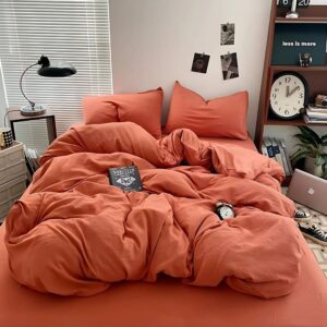 Parure de lit terracotta sur un lit double avec des coussins assortis. A droite, une étagère avec des objets dessus, un livre et un réveil sur le lit.