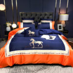 Parure de lit orange à motif cheval élégant avec le contour orange et le centre bleu marine. Sur un lit avec une tête de lit capitonnée noire.