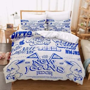 Une parure de lit Kpop NewJeans bleue et blanche avec des dessins de lapins kawaii et des écritures de style graffiti, installée sur un lit dans une chambre lumineuse avec des meubles en bois clair.