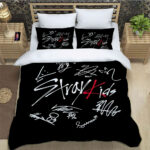 Une parure de lit Kpop Stray Kids noire et blanche avec des écritures rouges, composée d'une housse de couette et de deux oreillers assortis, installée dans une chambre moderne sur un cadre de lit en bois clair entouré de deux tables de nuit.