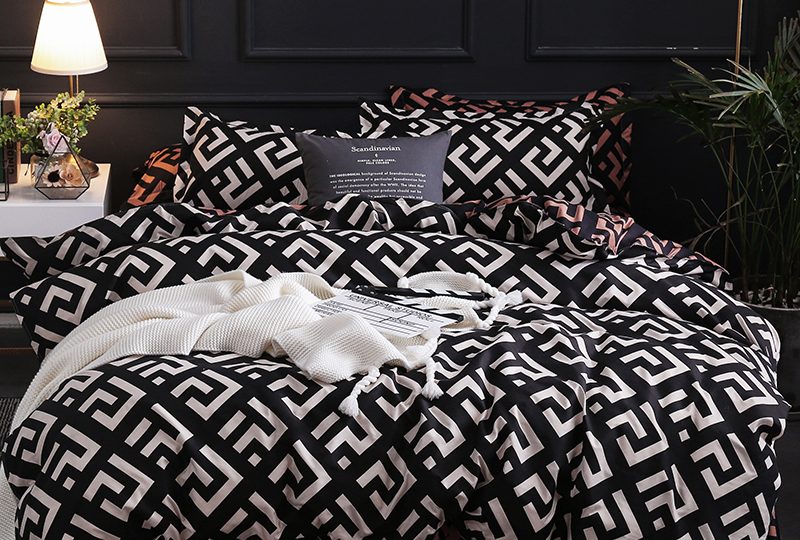 Parure de lit type scandinave de couleur noir et blanc avec des motifs carré avec un drap blanc posé dessus devant un mur noir