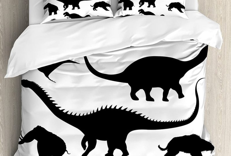 Dans une chambre le lit est décoré d'une parure avec des motifs de dinosaures noirs sur fonds blancs, les coussins sont assortis, la couette est en partie rabattue
