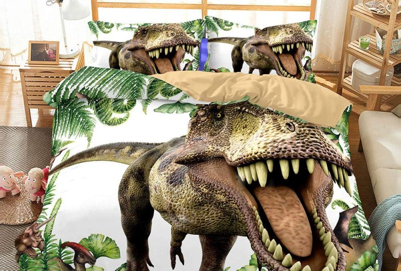 Dans une chambre le lit est décoré d'une parure avec énorme T-Rex en train de rugir, le reste de la couverture est décoré de feuille de forêt, les coussins sont assortis, à droite du lit il y a un banquette en bois avec les coussins blanc, et un meuble étagère en bois, à gauche du lit il y a une table de chevet en bois et des jouets