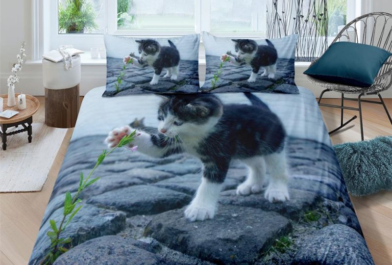 Parure de lit représentant un chat au pelage blanc et gris jouant avec une fleur sur des pavés de pierres
