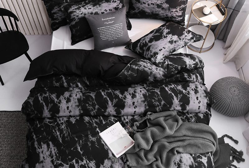 Parure de lit scandinave de type marbre de couleur noire et grise avec un livre ouvert dessus avec un coussin gris et une chaise noire à côté