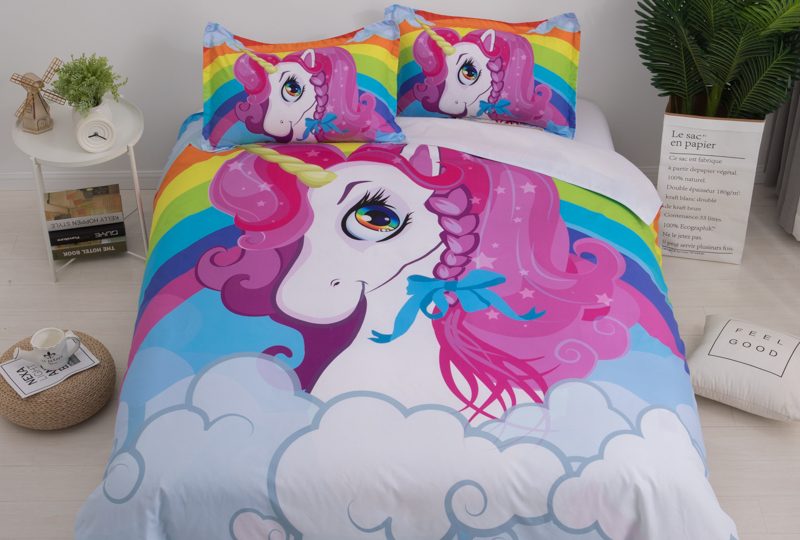 Parure de lit licorne avec un arc-en-ciel dans les nuages dans un chambre au style scandinave blanc et beige avec une petite table de chevet blanche