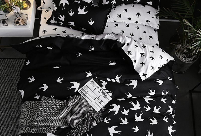 Parure de lit scandinave au motif d'hirondelle noire et blanche avec un drap gris et un livre ouvert posés dessus