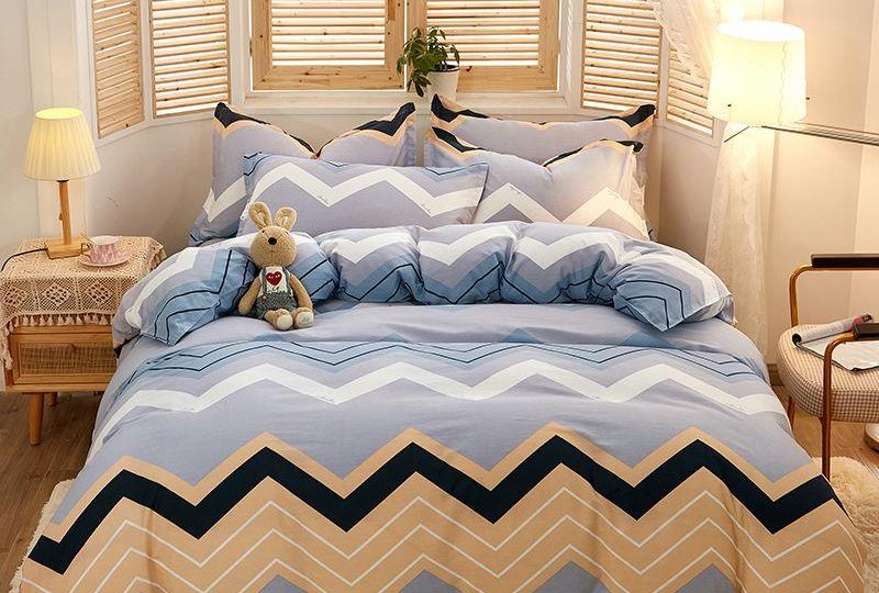 Parure de lit grise à rayures multicolores en zig zag. Bonne qualité, confortable et à la mode sur un lit dans une maison