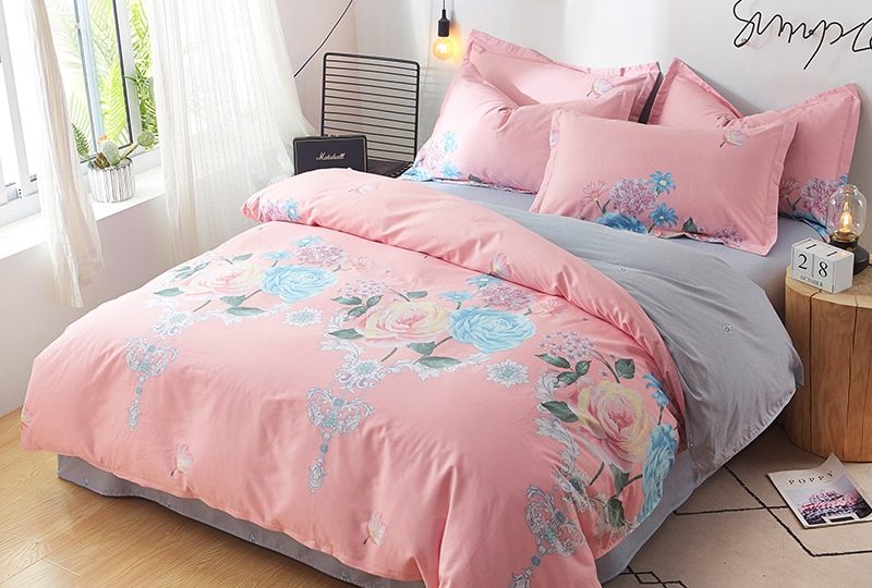 Parure de lit rose et grise avec imprimé fleuri. Bonne qualité, confortable et à la mode sur un lit dans une maison