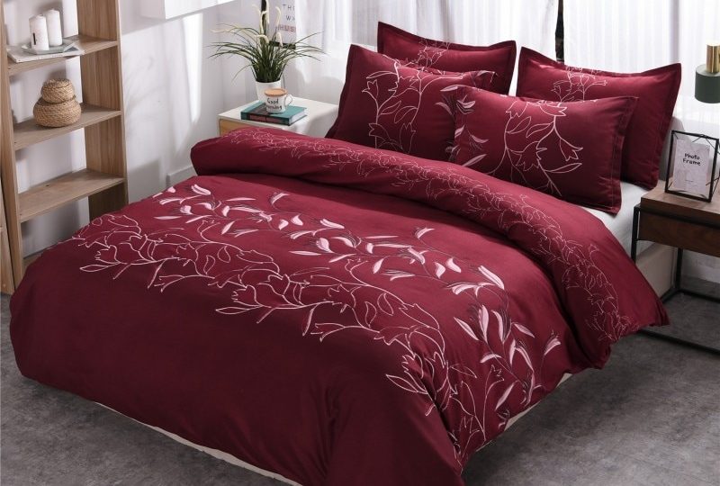 Parure de lit bordeaux à motif floral unique. Bonne qualité, confortable et à la mode sur un lit dans une maison