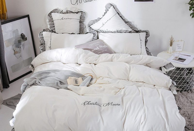 Parure de lit blanche contour gris. Bonne qualité, confortable et à la mode sur un lit dans une maison