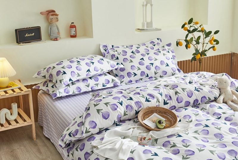 Parure de lit blanche à motif fleurs violettes. Bonne qualité, confortable et à la mode sur un lit dans une maison