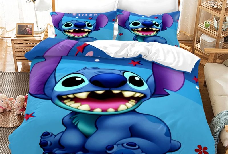Dans une chambre le lit est décoré d'une parure à l'effigie du personnage de Stitch, le reste de la couverture est bleu vif, les coussins sont assortis, à droite du lit il y a un banquette en bois avec les coussins blanc, et un meuble étagère en bois, à gauche du lit il y a une table de chevet en bois et des jouets