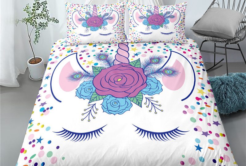 Parure licorne de couleur blanche représentant une licorne avec les yeux fermés avec une fleur de couleur violette et bleue juste en dessous de sa corne entouré d'étoiles multicolores dans une chambre blanche