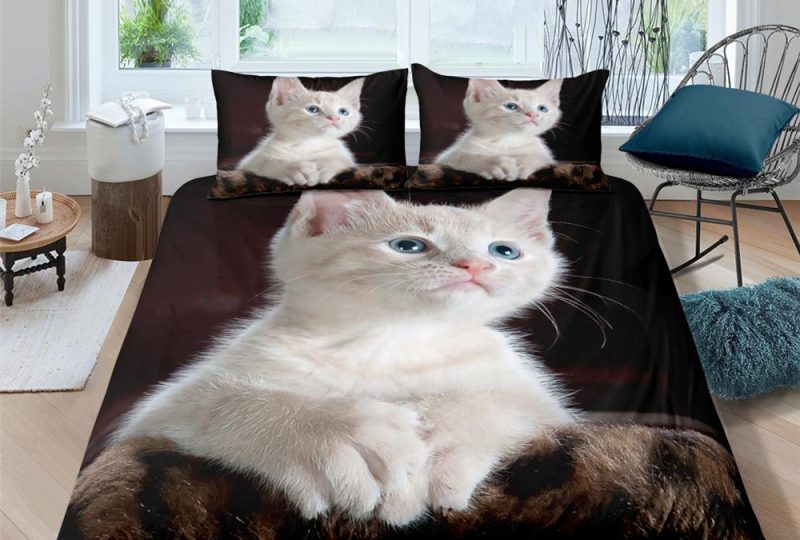 Parure de lit représentant un chat aux yeux bleus et pelage blanc posé sur un fond sombre dans une chambre avec parquet et mur blanc