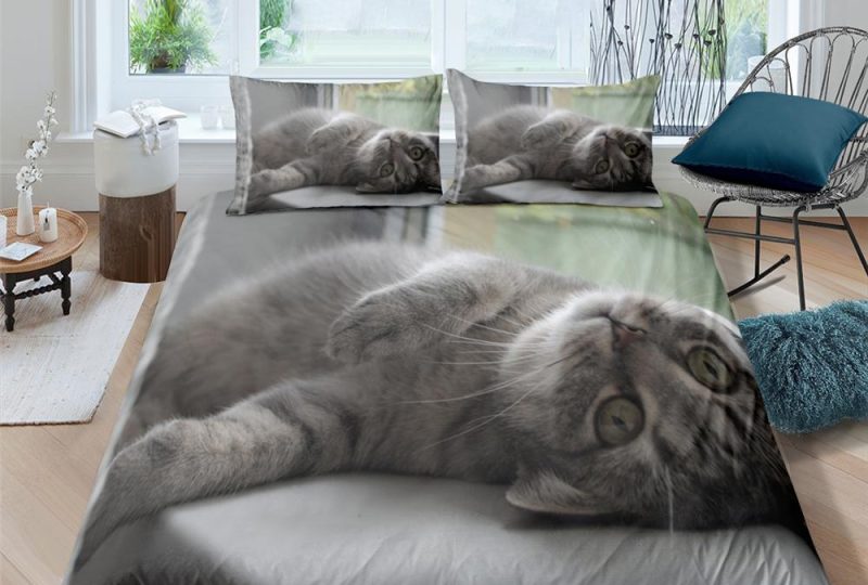 Parure de lit représentant un chat au pelage gris couché sur le dos sur un drap blanc