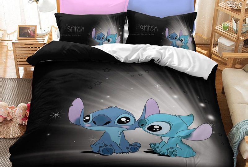 Dans une chambre le lit est décoré d'une parure à l'effigie des personnages de Stitch bébés, le reste de la couverture noir, les coussins sont assortis, à droite du lit il y a un banquette en bois avec les coussins blanc, et un meuble étagère en bois, à gauche du lit il y a une table de chevet en bois et des jouets