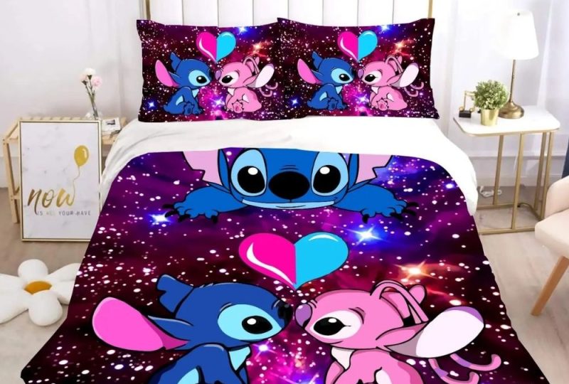 Parure de lit Sitch et Angel amoureux face à face avec un coeur rose et bleu au-dessus d'eux. Le fond ressemble à un ciel étoilé. Deux coussins assortis à la housse de couette se trouvent en haut du lit. Une table de chevet de chaque côté blanche et beige.