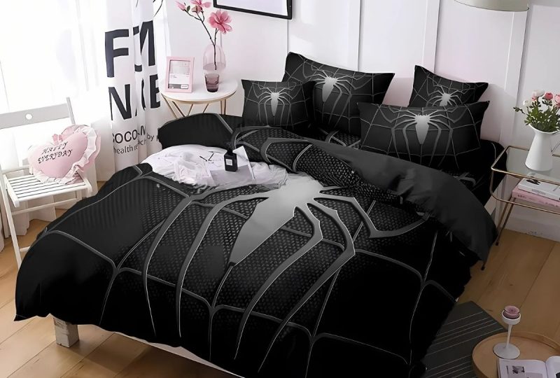 Parure de lit avec araignée de Spiderman blanche et grise sur fond noir. L'ensemble est sur un lit double avec des coussins assortis à la housse de couette.La décoration de la chambre est épurée dans les tons beige et blanc. Un tapis gris anthracite sur le coin droit de la photo.