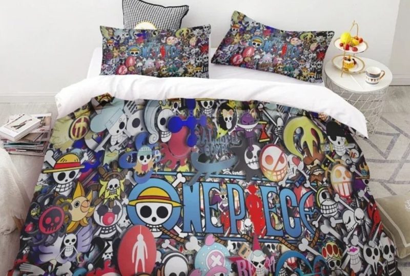 Parure de lit colorée One Piece avec tous les personnes du manga sur l'ensemble de la housse de couette et des coussins assortis. Posée sur un lit double avec un mur blanc en tête de lit, des livres posés à gauche et une petite table de chevet ronde à droite.