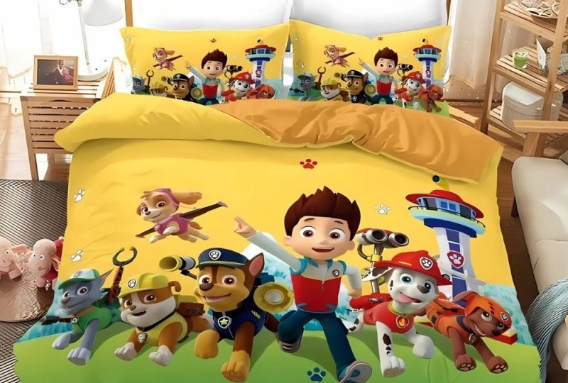 Parure de lit Pat'Patrouille avec l'équipe complète sur fond jaune avec de l'herbe sur lebas. Les deux coussins sont assortis à la housse de couette. Sur un lit double dans une chambre avec une grande fenêtre derrière.