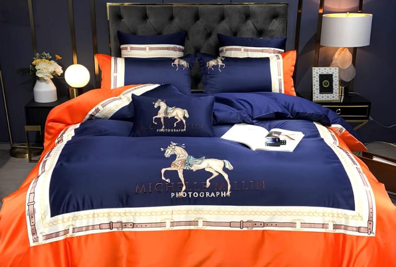 Parure de lit orange à motif cheval élégant avec le contour orange et le centre bleu marine. Sur un lit avec une tête de lit capitonnée noire.