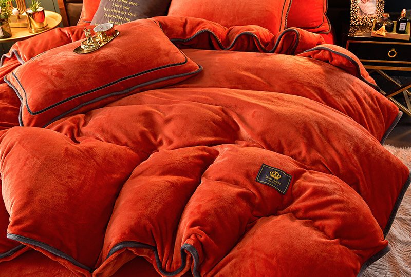 Parure de lit de couleur unie terracotta avec une tasse de thé dorée posée dessus, dans une chambre au ton sombre
