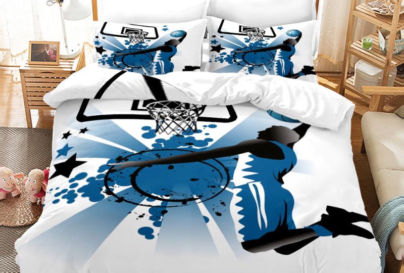 Parure de lit blanche et bleue avec la silhouette de Michael Jordan en train de marquer un panier de basket, dans une chambre avec une table de chevet en bois à gauche et un meuble étagère à gauche