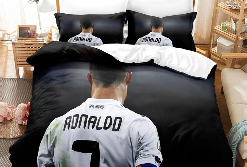 Parure de lit grise avec la photo de cristiano ronaldo vu de dos et dont on peut lire son nom sur le maillot de football , dans une chambre avec une table de chevet en bois à gauche et un meuble étagère à gauche