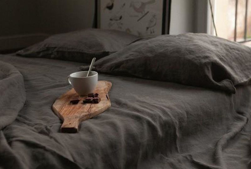 Dans une chambre le lit est recouvert d'une belle parure de lit en lit gris, avec les oreillers assorties , sur le lit est posée une petite planche de bois sur laquelle il y a une taille de boisson chaude