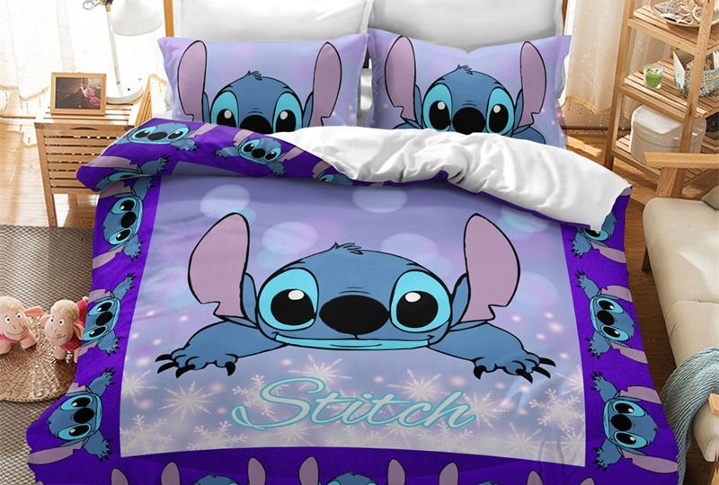 Dans une chambre le lit est décoré d'une parure à l'effigie du personnage de Stitch, le reste de la couverture est violet avec des tête du héro qui orne le tour du lit, les coussins sont assortis, à droite du lit il y a un banquette en bois avec les coussins blanc, et un meuble étagère en bois, à gauche du lit il y a une table de chevet en bois et des jouets